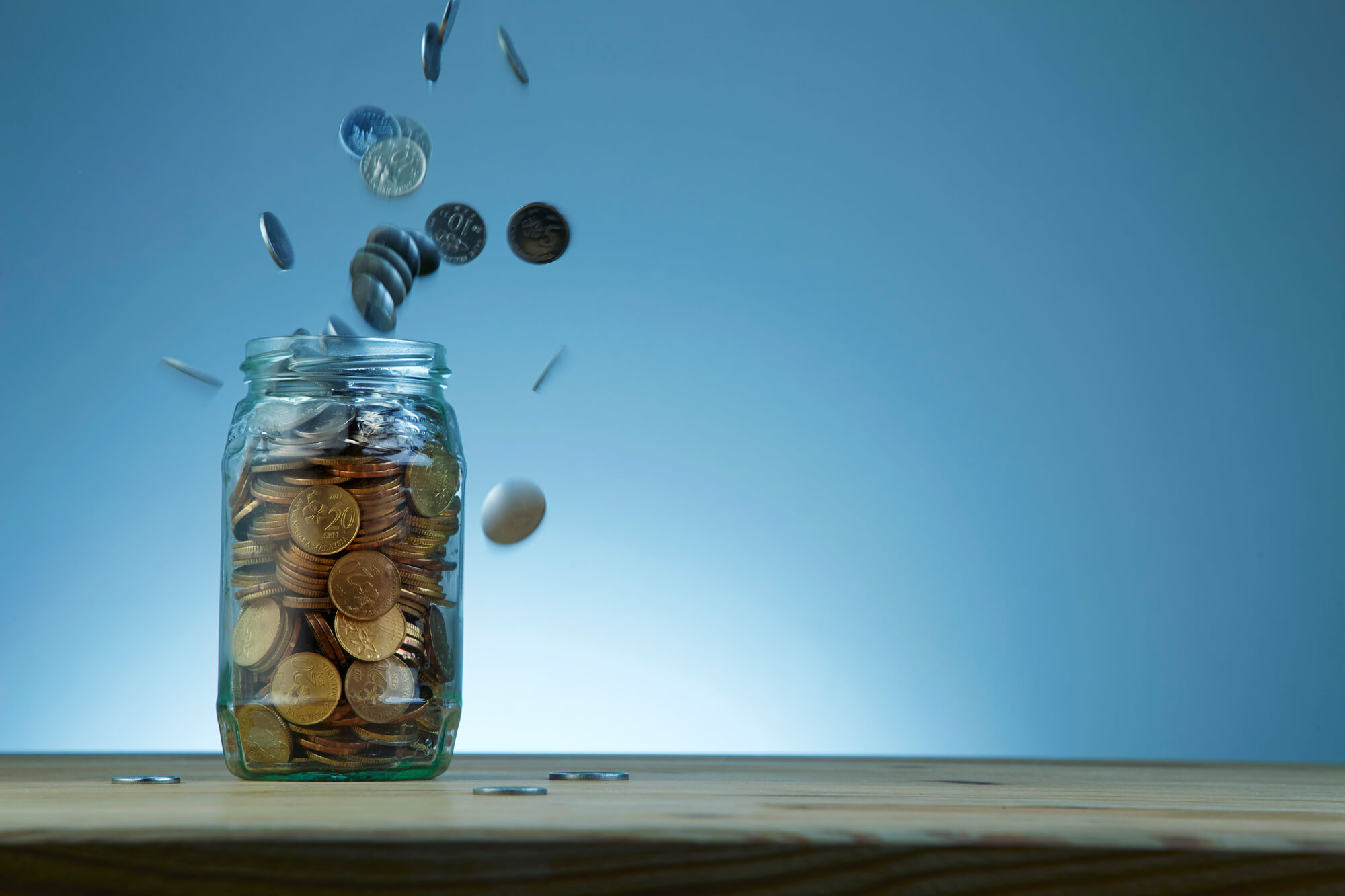 Coins falling into a glass jar with blue gradient background