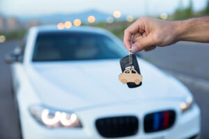 Hands holding new car keys with out-of-focus car in the background